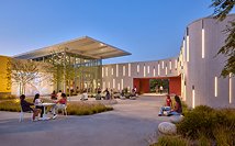 People sitting and talking outdoors near modern building with curved wall and tall windows at dusk.