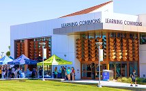 Modern building labeled Learning Commons with people and event tents outside on lawn.