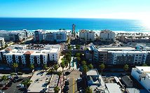 Aerial view of a coastal city with buildings, roads, palm trees, and the ocean in the background.